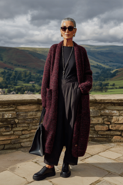 A long burgundy cardigan layered over an all-black outfit creates a simple but elevated travel look for cooler days 