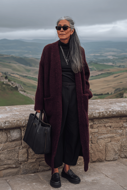 A long burgundy cardigan layered over an all-black outfit creates a simple but elevated travel look for cooler days 