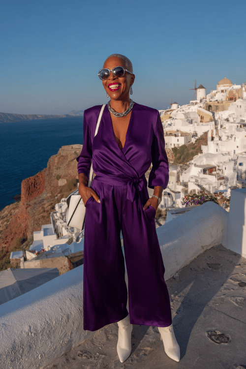 Chic vacation dinner outfit for women over 50 featuring a deep purple satin wrap jumpsuit styled with white pointed-toe boots