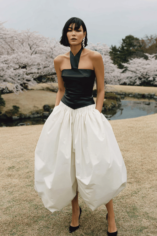 Woman in a black halter corset top and voluminous white trousers standing in a cherry blossom garden