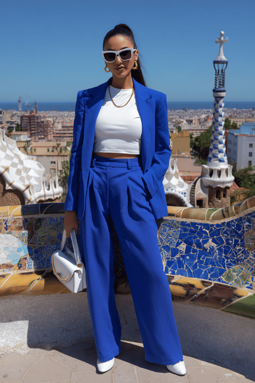 Woman wearing a bright blue pantsuit with a white crop top and white heels standing at Park Güell in Barcelona 