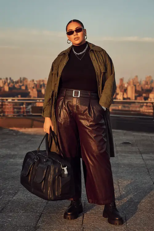 Woman wearing an olive trench coat, black turtleneck, burgundy leather culotte pants, and combat boots with sunglasses, 