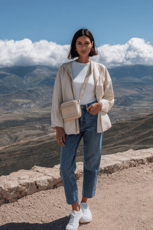 woman with a sleek dark brunette bob worn straight and casual travel outfit consisting of a fitted white ribbed top tucked into relaxed straight-leg mid-wash blue denim jeans 