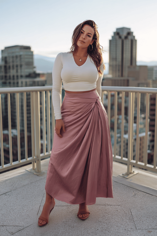 a curvy woman wearing a flowing floor-length silk wrap skirt in warm dusty rose paired with a fitted long-sleeve mock-neck top in soft ivory, minimalist leather sandals