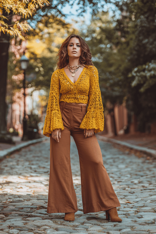 a curvy woman wearing a mustard yellow crochet top with billowing sleeves paired with wide-leg earth-tone linen trousers, suede ankle boots, and layered pendant necklaces