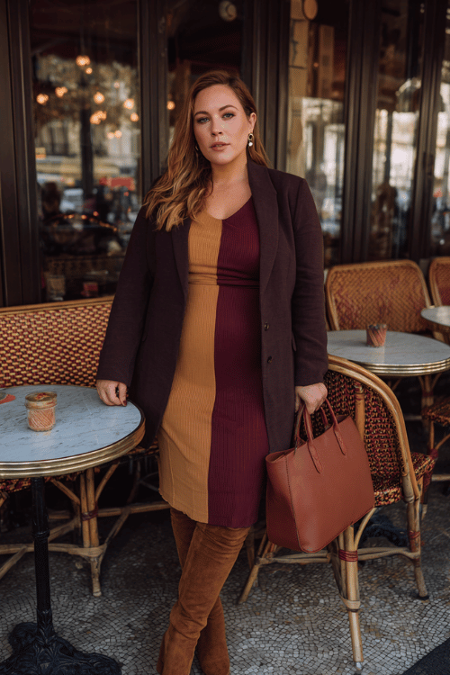 a plus-size midsize woman wearing a bold color-blocked midi dress combining deep burgundy and warm camel panels with long sleeves and a defined waist