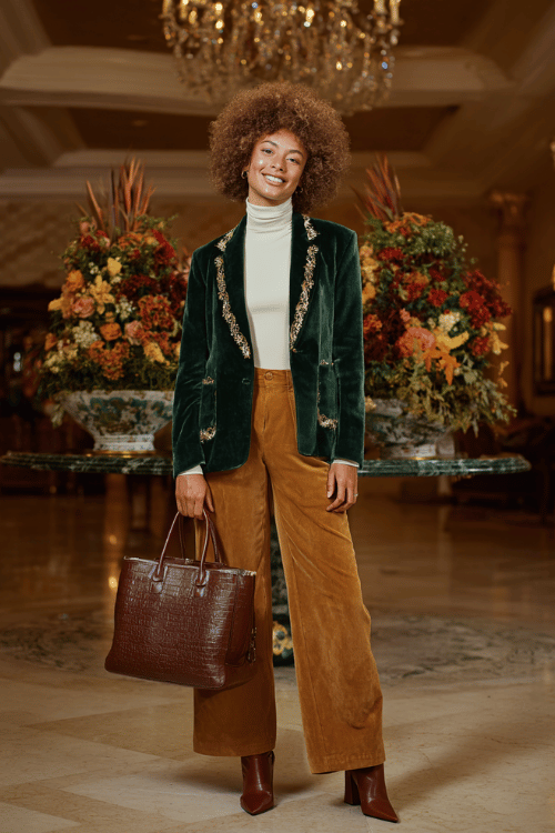 a plus-size woman over 50 with a bold silver afro wearing a luxurious deep forest green velvet blazer with gold embroidered lapels over a crisp ivory turtleneck and wide-leg trousers