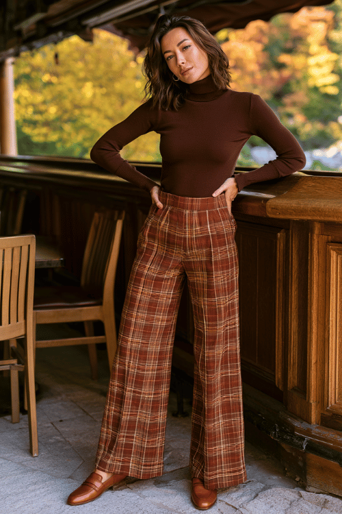 a woman dressed in a chocolate brown mock-neck fitted sweater, high-waisted plaid wide-leg trousers in rust and tan tones, and brown leather loafers