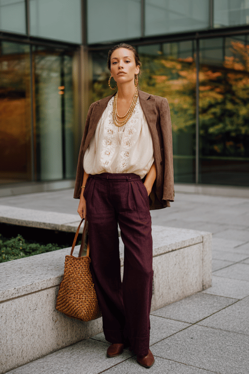 a woman in a refined boho ensemble a loose embroidered blouse in warm cream tucked into high-waisted wide-leg trousers in deep plum layered with a fitted suede blazer