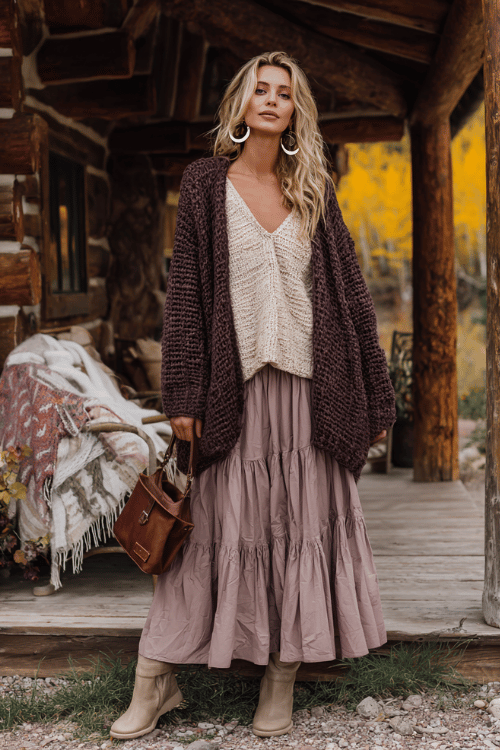 a woman in a relaxed oversized boho pullover in a soft chunky knit of warm cinnamon and cream tones, paired with a flowing tiered skirt in muted dusty mauve