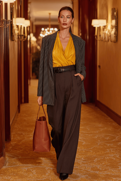 a woman wearing a bold mustard yellow wrap blouse tucked into high-waisted wide-leg trousers in rich espresso brown, layered with a longline charcoal grey blazer