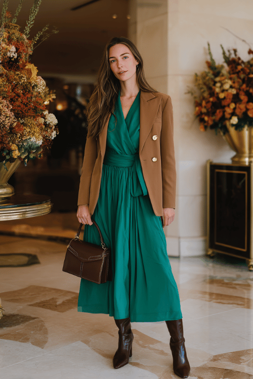 a woman wearing a rich emerald green long-sleeve wrap dress with a beautifully cinched waist and flowing midi skirt, layered with a tailored camel blazer with gold button details 