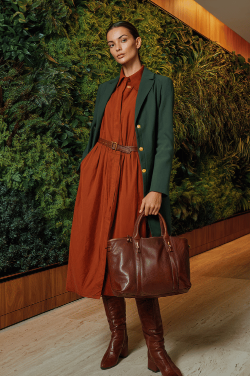 a woman wearing a warm terracotta long-sleeve shirt dress with a relaxed belted waist and midi length, layered with a fitted forest green blazer with subtle gold hardware 