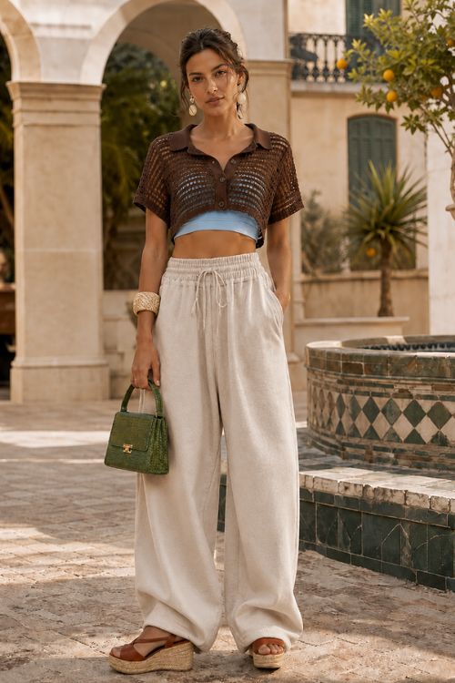 A brown crochet cropped polo top with a blue bandeau, beige drawstring wide-leg pants, wedge sandals, and a green handbag