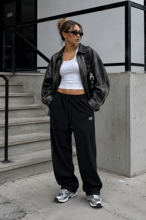 A woman wears a black beanie with an oversized gray bomber jacket, a fitted black top, olive green sweatpants, and chunky black sneakers