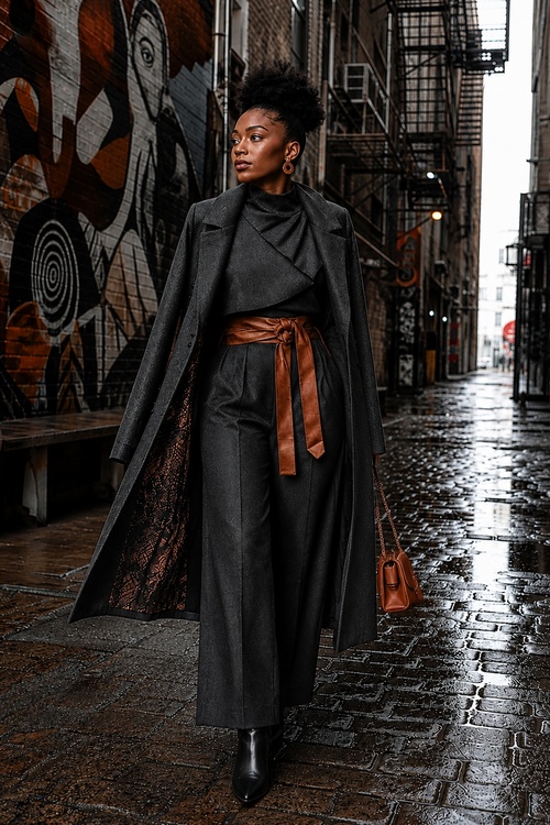 Woman in a charcoal layered outfit with a long coat walking through a rainy city alley