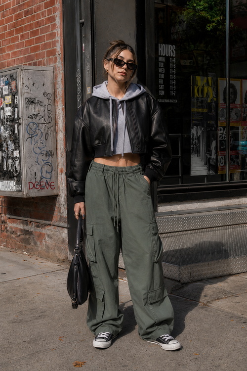 Woman in a cropped leather jacket, cargo pants, and black Converse.