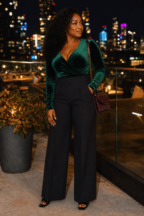 Woman in a green velvet wrap top with black wide-leg pants on a rooftop at night
