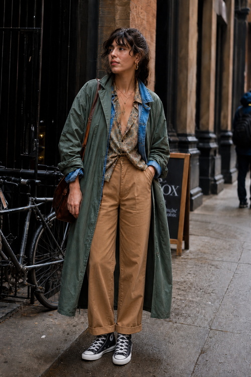 Woman in an olive coat, tan trousers, and black Converse.