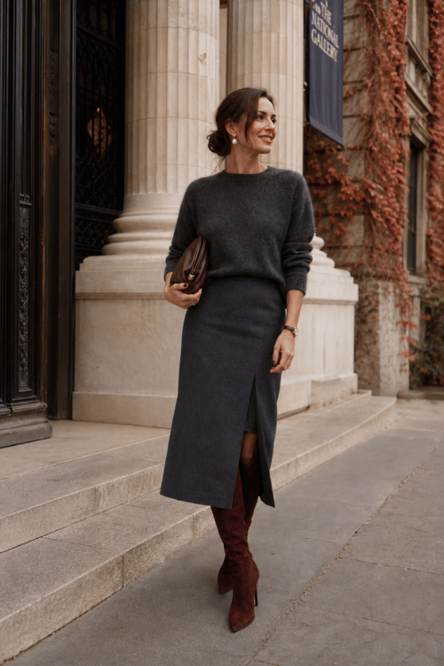 Woman wearing a charcoal knit sweater dress with a side slit, burgundy suede knee-high boots, and a burgundy leather clutch.