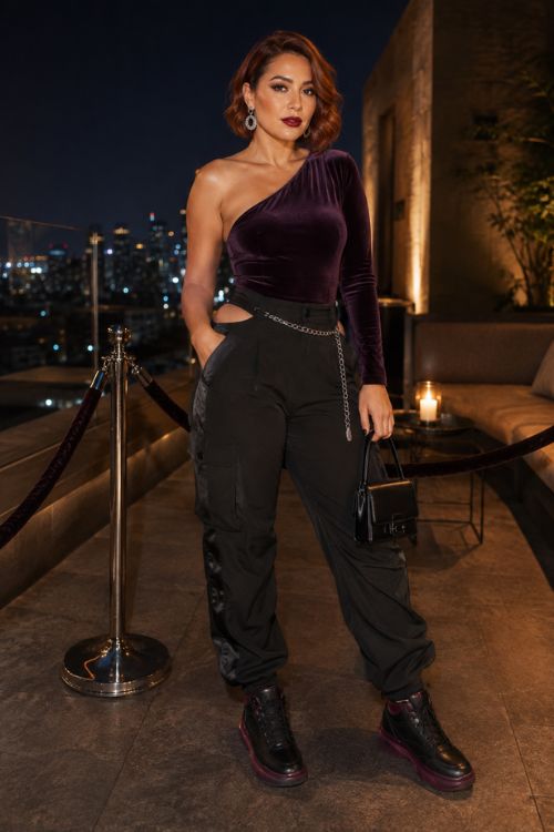 a woman in a plum velvet one shoulder top and a black pants, black boots