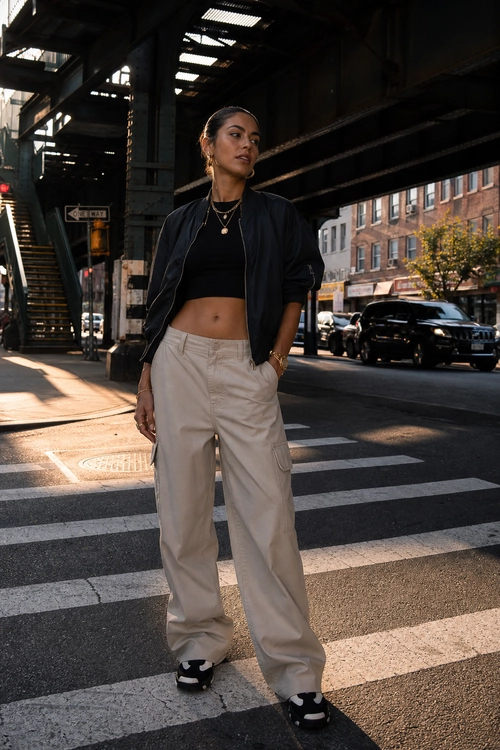 Black Bomber Jacket and Cargo Pants A streetwear outfit featuring a black bomber jacket, black cropped top, beige cargo pants, and black-and-white sneakers.
