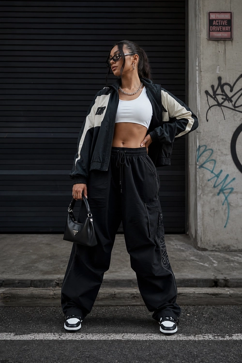 Black and Cream Streetwear Outfit A black and cream jacket layered over a white cropped tank top with black cargo pants, sneakers, sunglasses, a chain necklace, and a small black handbag.