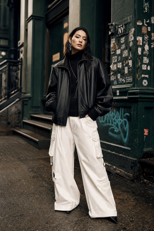 Black Leather Jacket with White Cargo Pants A woman wears a black leather jacket over a black high-neck top with white wide-leg cargo pants and black pointed footwear.