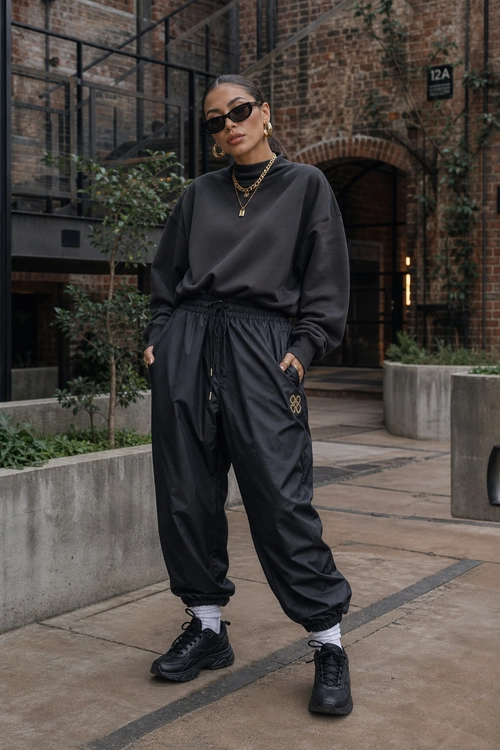 Black Streetwear Jogger Outfit A monochrome black streetwear outfit featuring an oversized sweatshirt, jogger pants, sneakers, sunglasses, and layered gold jewelry.