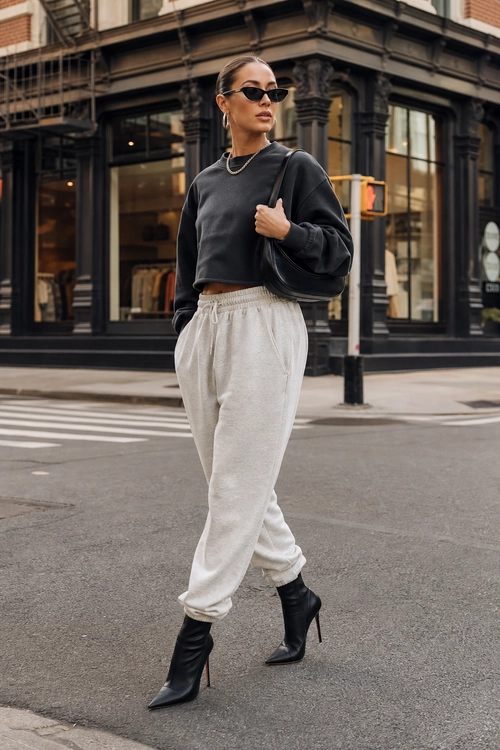 Black Sweatshirt and Gray Jogger Outfit Street style outfit featuring a cropped black sweatshirt, light gray jogger pants, black heeled boots, sunglasses, and a shoulder bag.