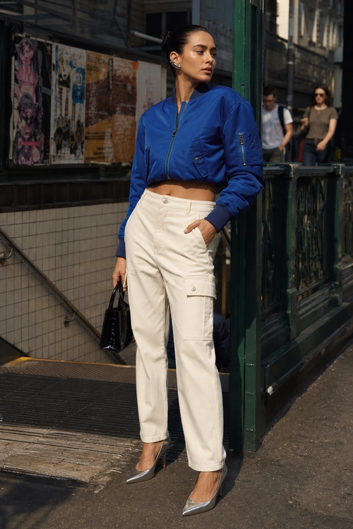 Blue Bomber Jacket and Ivory Cargo Pants A woman wears a cropped blue bomber jacket with ivory cargo pants, metallic pointed-toe shoes, and a black handbag.