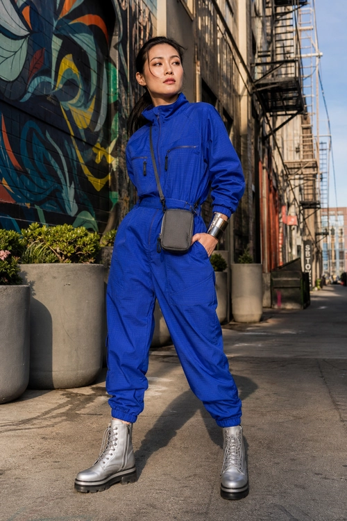 Blue Utility Jumpsuit Look A person wears a cobalt blue long-sleeve jumpsuit with silver combat boots, a gray crossbody bag, and a metallic cuff bracelet.
