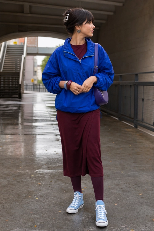 Blue Windbreaker and Burgundy Casual Outfit A woman wears a bright blue windbreaker over a burgundy top with burgundy bottoms, leggings, light blue sneakers, and a purple shoulder bag.