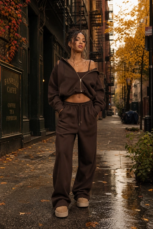 Brown Cropped Hoodie and Joggers A person wears a brown cropped zip-up hoodie, matching jogger pants, beige shoes, and a delicate necklace on a wet city street.