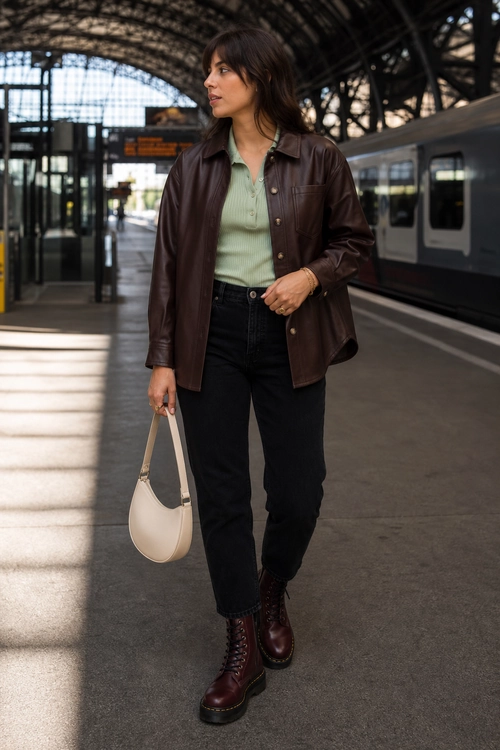 Brown Leather Jacket and Black Jeans Outfit A woman wears a brown leather jacket over a mint green collared top with black jeans, burgundy lace-up boots, and a cream shoulder bag.