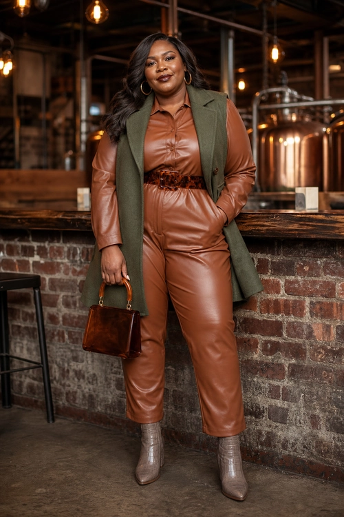 Brown Leather Jumpsuit Look A woman wears a brown leather jumpsuit with an olive sleeveless vest, ankle boots, hoop earrings, and a small structured handbag.