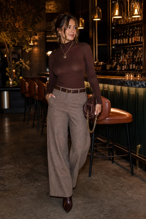 Brown Turtleneck and Wide-Leg Trousers A woman wears a fitted brown turtleneck with taupe wide-leg trousers, a dark belt, pointed boots, and a small chain-strap handbag.