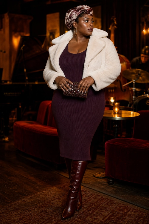 Burgundy Dress with Cream Coat A woman wears a burgundy ribbed midi dress with a cream plush coat, matching tall boots, a patterned headwrap, hoop earrings, and a beaded clutch.