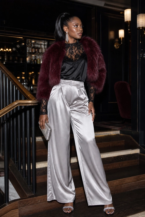 Burgundy Fur and Silver Satin A woman wears a burgundy faux fur jacket over a black lace and satin top with silver satin wide-leg trousers, embellished heels, dangling earrings, and a silver clutch.