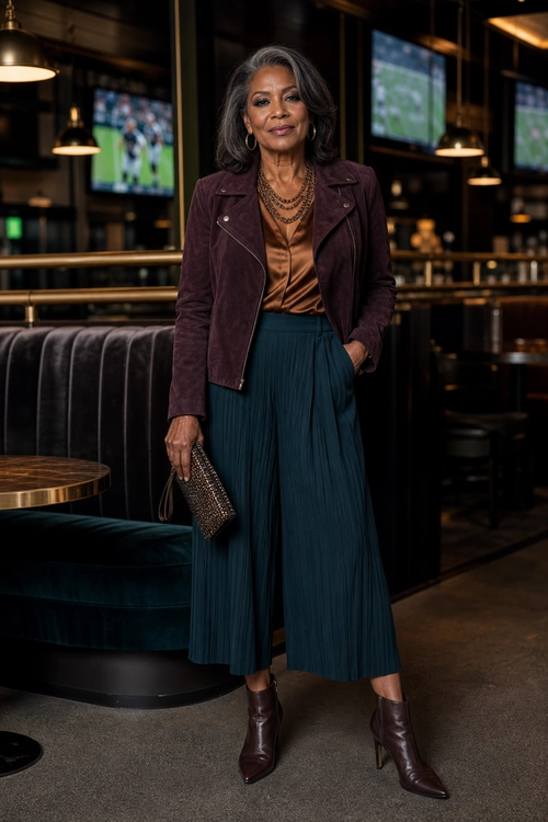 Burgundy Jacket and Teal Culottes A woman wears a burgundy jacket over a bronze satin top with teal pleated culottes, ankle boots, layered necklaces, hoop earrings, and a clutch.