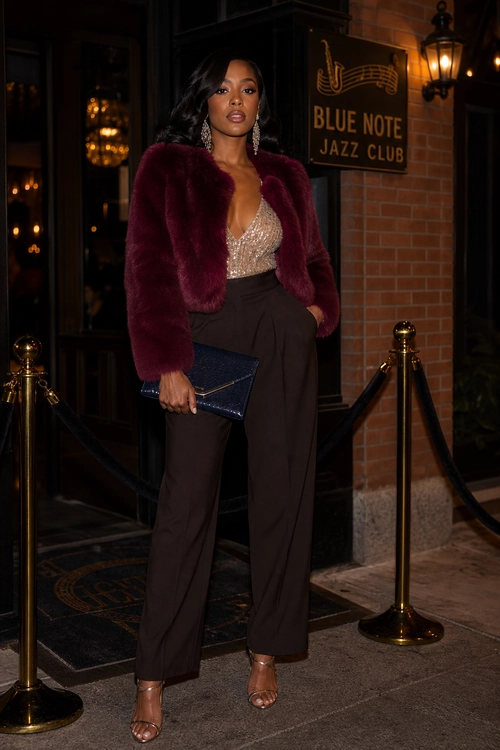 Burgundy Jacket and Wide-Leg Evening Outfit A woman wears a burgundy fur-textured jacket over a champagne embellished top with dark brown wide-leg trousers, a navy clutch, statement earrings, and strappy heeled sandals.