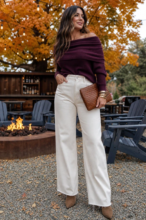 Burgundy Sweater and Ivory Jeans A woman wears an off-the-shoulder burgundy sweater with ivory wide-leg jeans, tan pointed shoes, gold bangles, and a woven brown clutch outdoors.