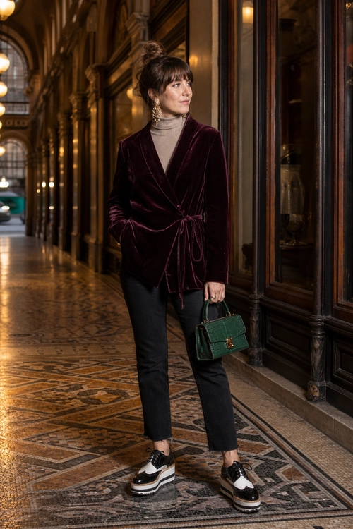 Burgundy Velvet Wrap Jacket Outfit A woman wears a burgundy velvet wrap jacket over a taupe turtleneck with cropped black pants, platform sneakers, and a green handbag.