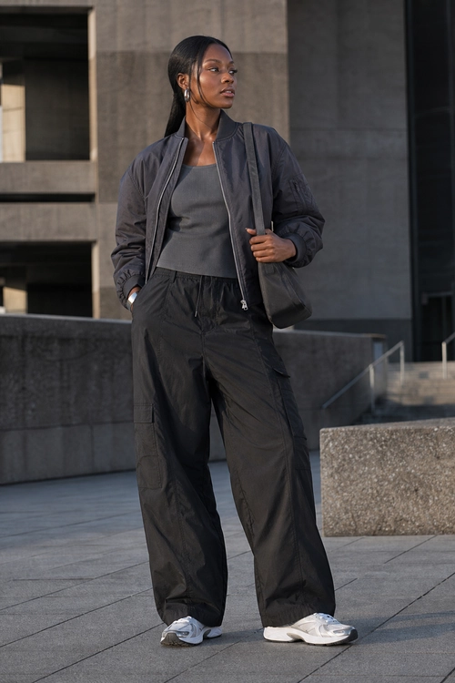 Charcoal Bomber Jacket and Wide-Leg Pants Street-style outfit featuring a charcoal bomber jacket, dark gray tank top, wide-leg utility pants, black shoulder bag, and white sneakers.
