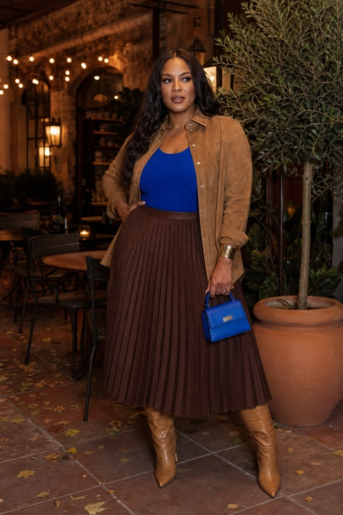 Cobalt Top and Pleated Skirt A woman wears a cobalt blue top with a tan overshirt, brown pleated midi skirt, tan boots, and a small blue handbag.