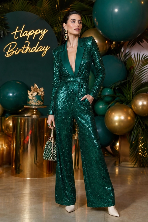 Emerald Sequin Jumpsuit A woman wears an emerald green sequin jumpsuit with wide legs, white pointed shoes, and a small beaded handbag at a birthday celebration.