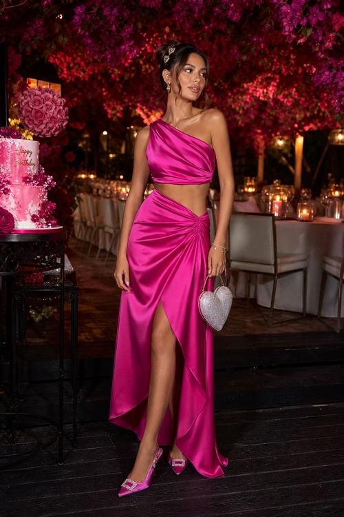 Fuchsia Satin Two-Piece Evening Outfit A fuchsia satin one-shoulder crop top and draped maxi skirt styled with pink heels and a silver heart-shaped handbag.