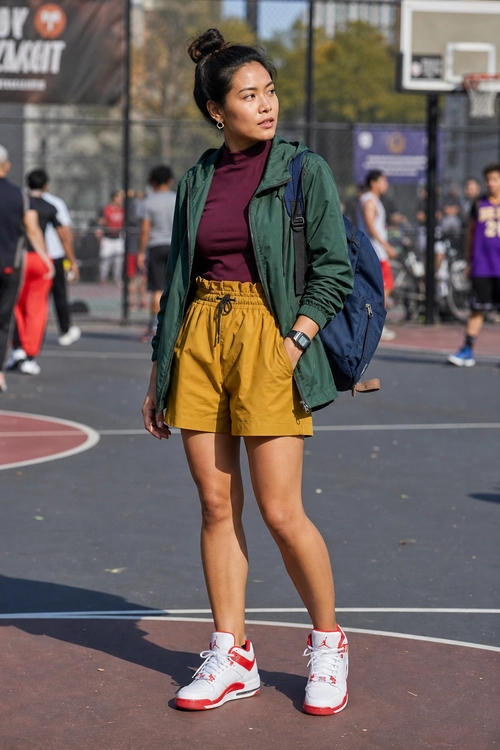 Sporty Green Jacket and Yellow Shorts Outfit A sporty outfit featuring a green hooded jacket, burgundy top, mustard yellow drawstring shorts, white and red high-top sneakers, and a blue backpack.