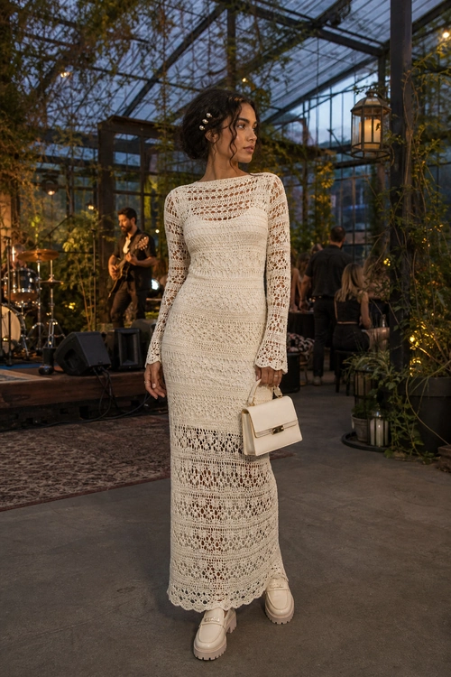 A woman wears an ivory long-sleeved crochet maxi dress with chunky white platform shoes and a structured cream handbag.