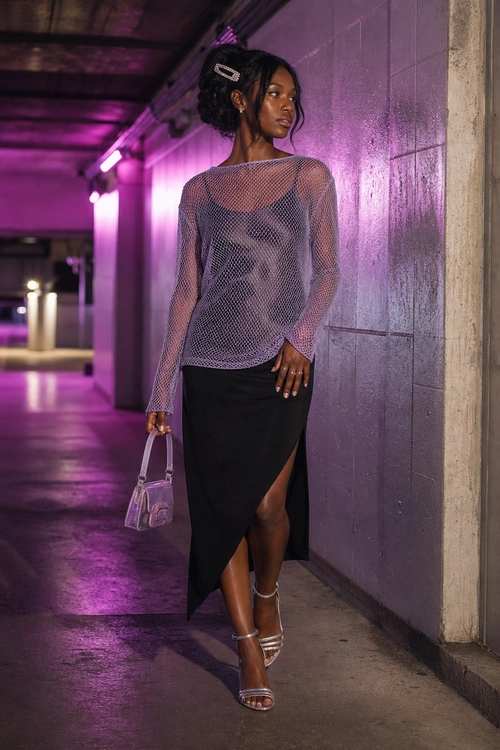 Lavender Mesh Top and Black Slit Skirt A woman wears a lavender sheer mesh long-sleeve top with a black asymmetrical slit skirt, silver strappy heels, and a small metallic handbag.